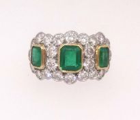 A fine emerald and diamond ring set with three emeralds within an arrangement of twenty four