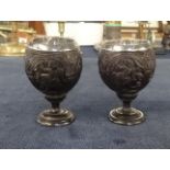 A pair of unusual carved coconut table salts or egg cups mounted with silver?, decoration of