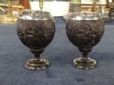 A pair of unusual carved coconut table salts or egg cups mounted with silver?, decoration of