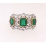 A fine emerald and diamond ring set with three emeralds within an arrangement of twenty four