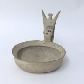 A pottery cup with a low circular body and a raised handle in the form of a stylised human figure,