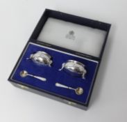 A pair of silver table salts with blue glass liners and spoons by Carrington, London, cased.