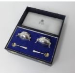 A pair of silver table salts with blue glass liners and spoons by Carrington, London, cased.