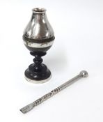 A silver incense holder with a silver bombilla on a dark wood base.