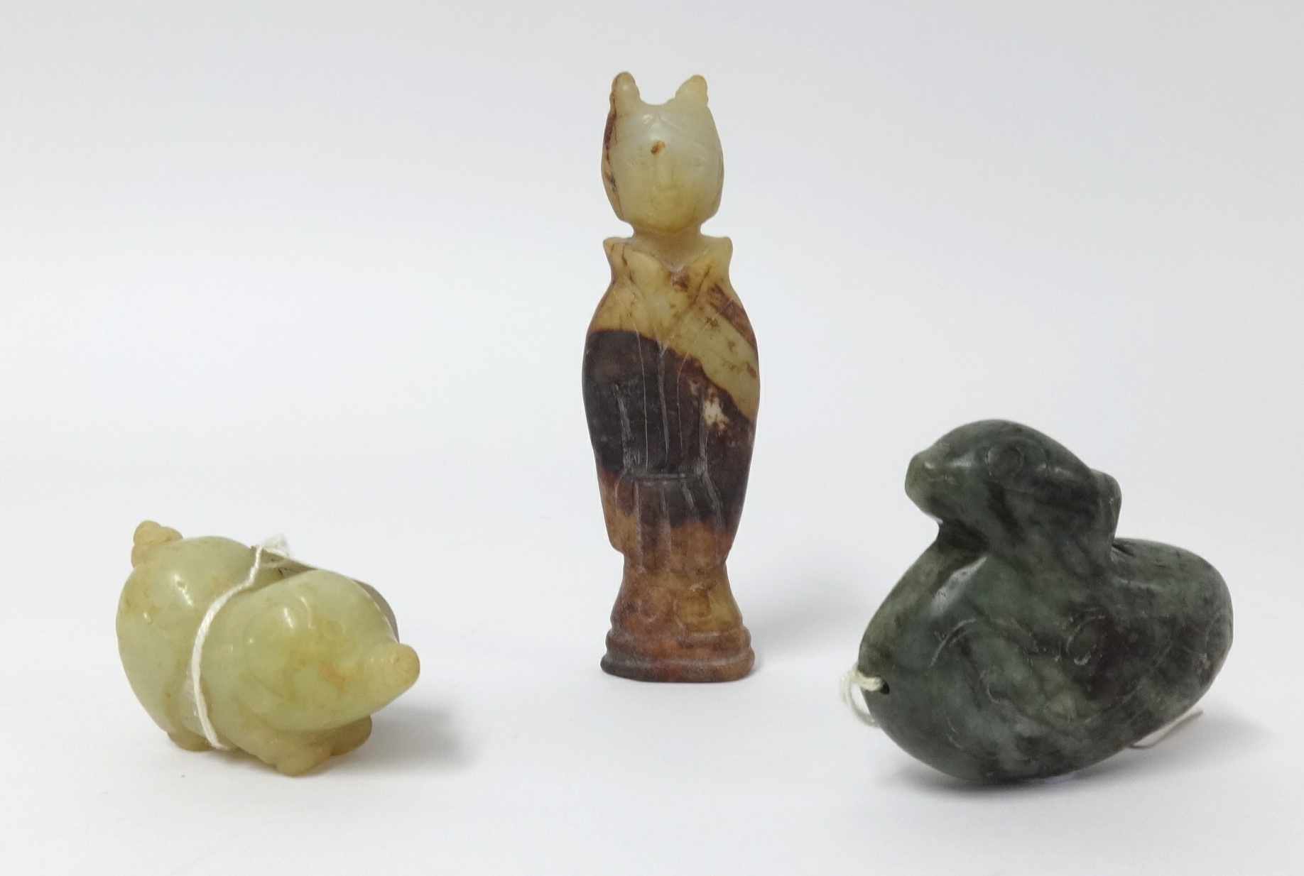 An oriental carved jade figure, a carved pig and dark green jade duck pendant, the tallest 7cm (3).
