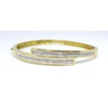 A 14ct yellow gold crossover bangle, channel set with diamonds.