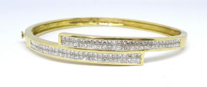 A 14ct yellow gold crossover bangle, channel set with diamonds.