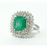 An emerald and diamond cushion shaped 3 row cluster ring, comprising central emerald cut emerald