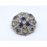 An 18ct white gold hand crafted designer brooch, consisting of a scallop circle pave set with a