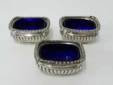 Three Victorian silver sarcophagus shaped table salts with blue glass liners