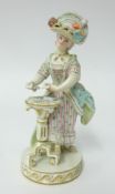 A late 19th century Meissen porcelain figure of a standing woman in 19th century costume by a tripod