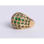 An 18ct yellow domed gold dress ring, comprising six rows of small round cut emeralds graduated to