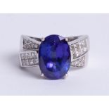 White metal large oval Tanzanite solitaire stone in four claw setting with diamond set crossover