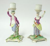 A pair of 18th century Meissen candlesticks, modelled as a gallant and his maiden holding baskets on