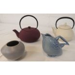 A metal teapot in a purple anodized finish, a cream ceramic teapot with black metal handle, a studio