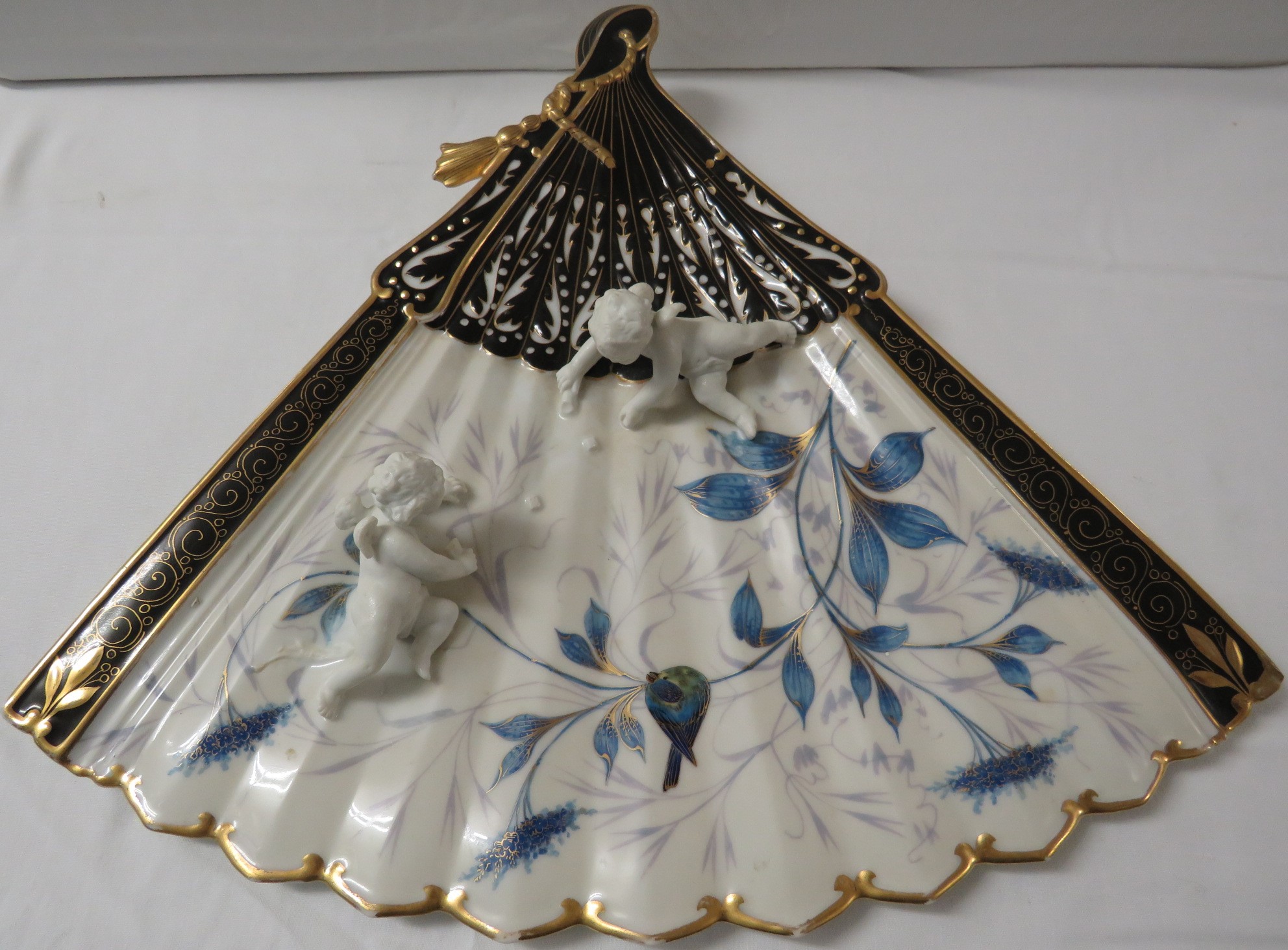 Porcelain wall plaque modelled as a fan with two moulded cherubs, black enamel and gilding and