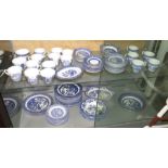 TWO SHELVES OF ASSORTED BLUE AND WHITE WILLOW PATTERN CHINA INCLUDING CUPS AND SAUCERS, BOWLS AND