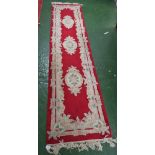 RED GROUND EMBOSSED FLOOR RUNNER WITH THREE FOLIATE MEDALLIONS AND TASSELED ENDS