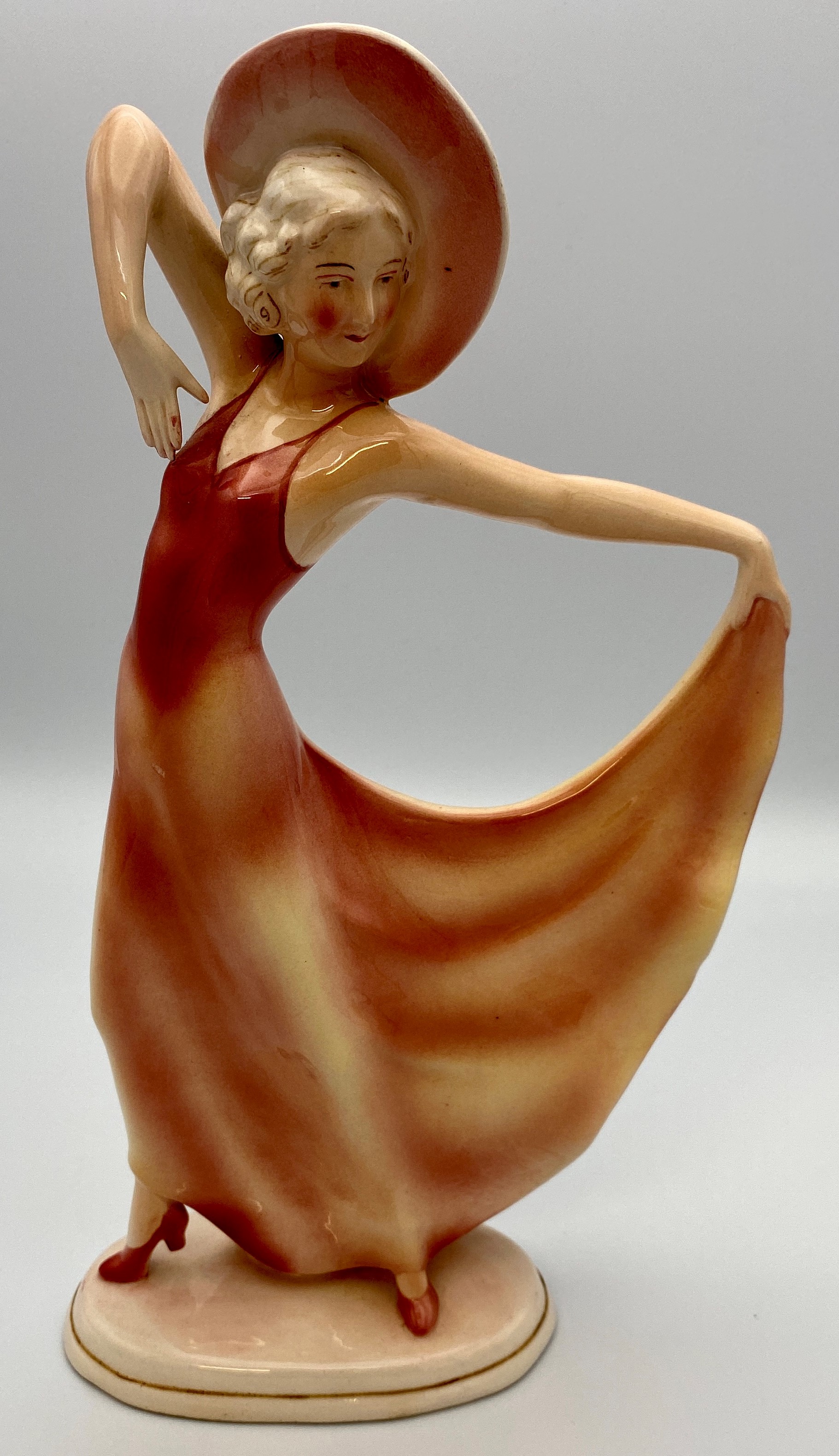 German Art Deco "Katshute" ceramic figure of woman in hat holding hem of pink dress, on oblong base,