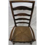 Early 19th century oak framed nursing chair, ladder back with scrolled arms and rush seat, on
