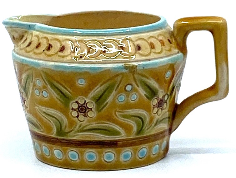 A small Linthorpe Pottery milk jug, pale treacle glaze with blue dots and lines and a band of