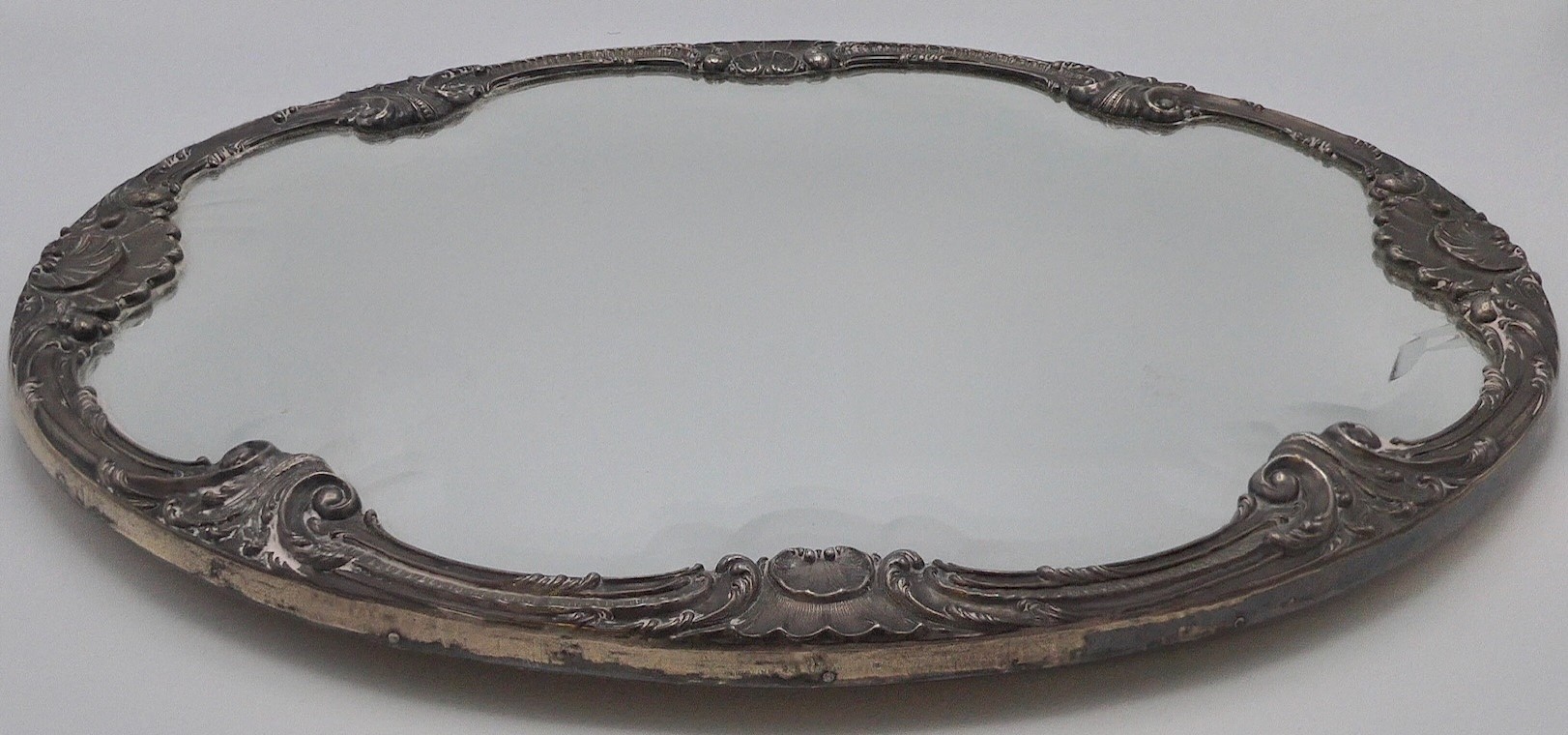 A shaped oval mirror tray with bevelled glass and mounted with a white metal frame decorated with