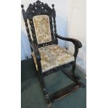 A carved ebonised rocking chair with pale foliate upholstered seat and back cushion, the back carved