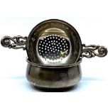Silver tea strainer and stand, the strainer with embossed scrolled handles, marks for Birmingham,