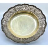 A white metal circular fruit dish with a pierced foliate scrolled border, standing on three