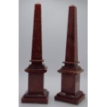 A pair of composition pylons or obelisks on square stepped plinths in a red marble-effect gloss