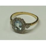 YELLOW METAL RING SET WITH AN OVAL CUT AQUAMARINE COLOUR STONE (ABOUT 8MM X 5MM) IN A HALO OF