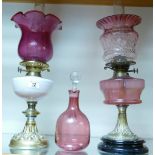 A brass and cranberry glass oil lamp: together with a white and cranberry oil lamp and a cranberry