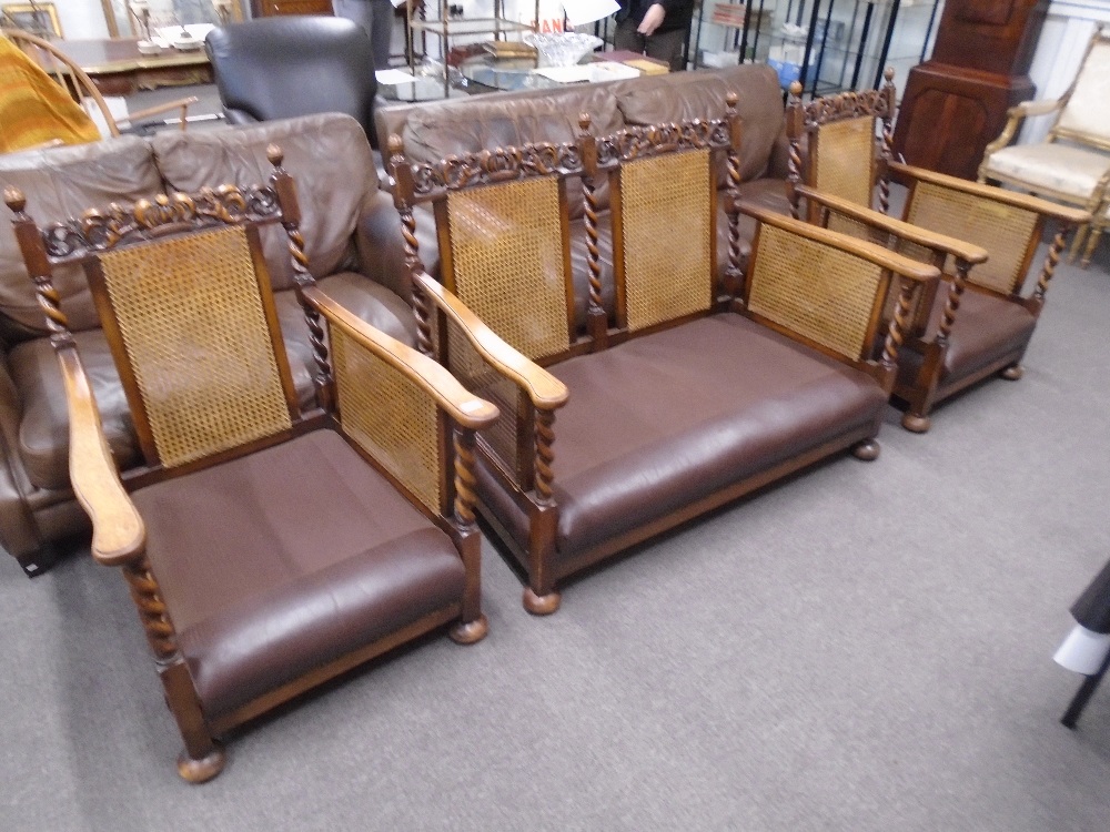 A pair of 1930's oak bergere armchairs and matching two seat settee with barley twist supports and