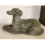 A composition stone hound, the resting dog on plinth with curled tail. (24in)