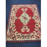 A floral rug woven with oval medallion and bows on a burgundy field framed by floral scrolled border