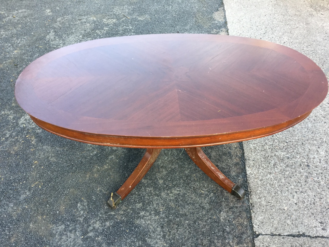 An oval mahogany coffee table, the crossbanded quarter veneered top on bulbous turned column, raised