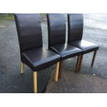 A set of three modern faux leather dining chairs, with high backs above sprung seats, raised on