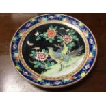 A porcelain charger decorated in an oriental palette with exotic birds, prunus blossom and