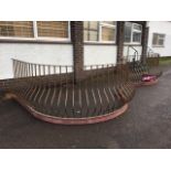 A serpentine fronted wrought iron balustrade, the square bombé spindles beneath rectangular