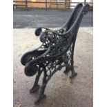 A pair of cast iron bench ends with scrolled backs and arms centering on floral roundels, with