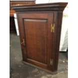 A Georgian oak corner cabinet with moulded dentil cornice above a fielded panel door enclosing