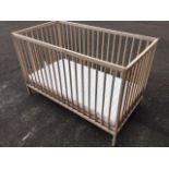 An unused 4ft beech cot with spindles to sides in rectangular frames, having ribbed mattress on