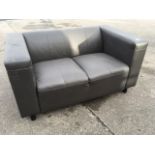A faux-leather two-seater sofa, with padded back and square platform arms, raised on tubular