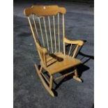 A beech rocking chair with shaped back rail on spindles with angled arms above a laminated seat,