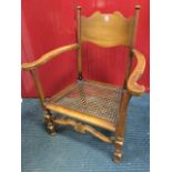 A cane seated armchair with shaped back panel on turned columns with curved platform arms, the