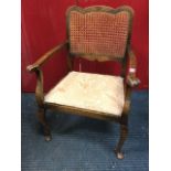 A Queen Anne style armchair with shaped cane back above an upholstered seat with outswept handrests,
