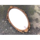 An oval mirror in ropetwist gilt frame with leaf scrolled mounts beneath floral crest.