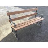 A cast iron garden bench with wood slatted back and seat, the ends with scrolled arms, and pierced