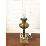 A Victorian style brass oil lamp with fluted column beneath bun shaped reservoir, on square leaf