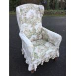 An upholstered Edwardian wing armchair with later linen loose covers, the padded back above sprung